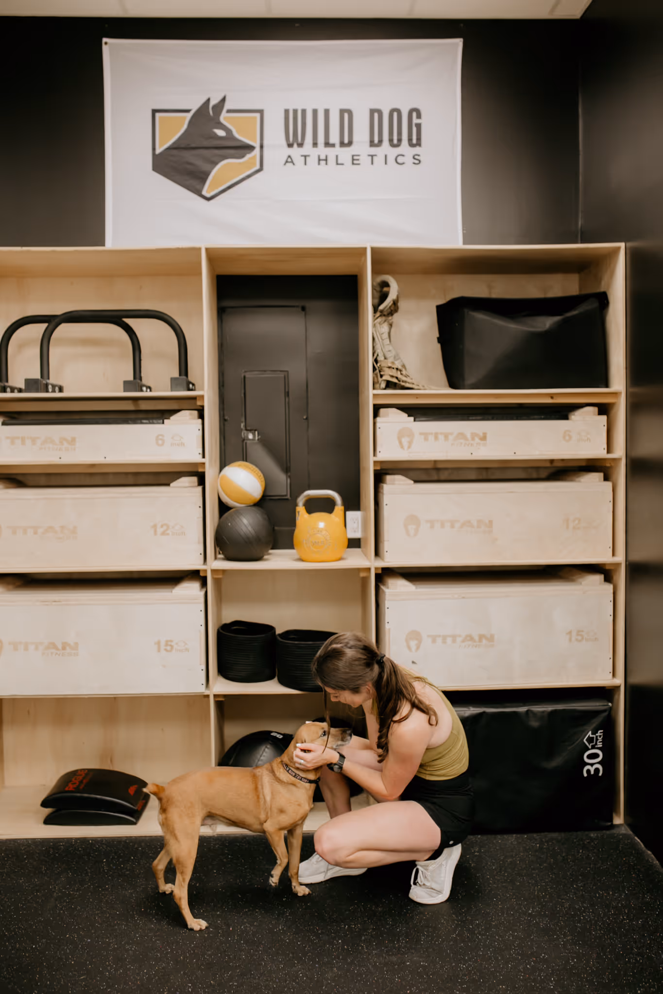Coach Abby of Wild Dog Athletics poses in her athletic training gym with her dog.