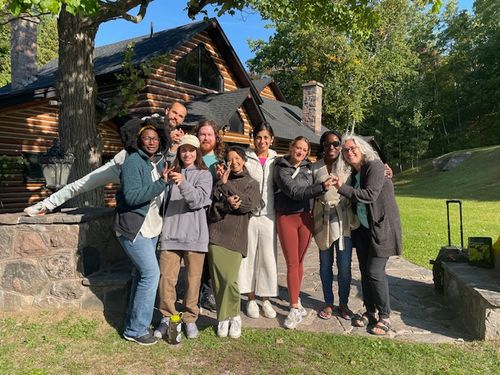 Nine members of the Connect Project Team stand outside as a group. Behind them is a cabin and a field with trees.