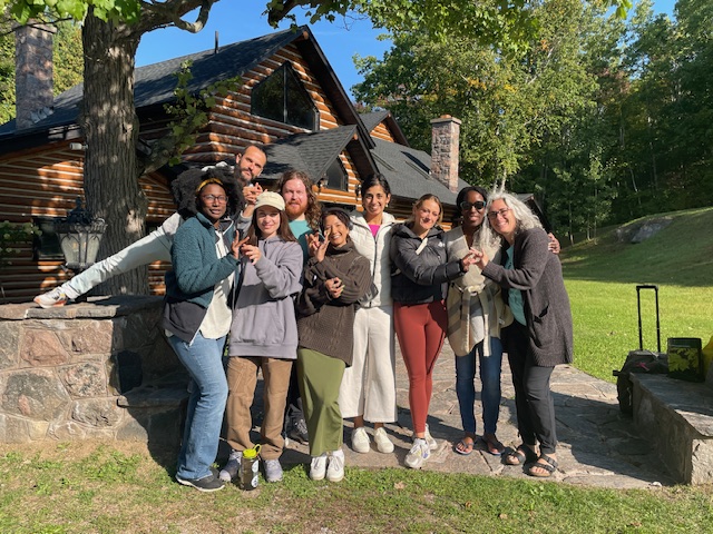 Nine members of the Connect Project Team stand outside as a group. Behind them is a cabin and a field with trees.