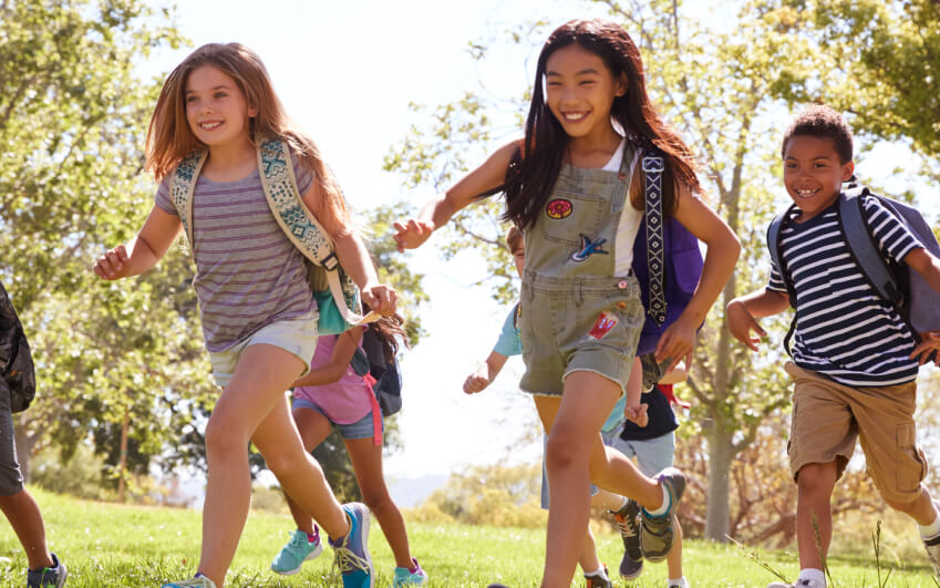 Children with school bags running in a park together.