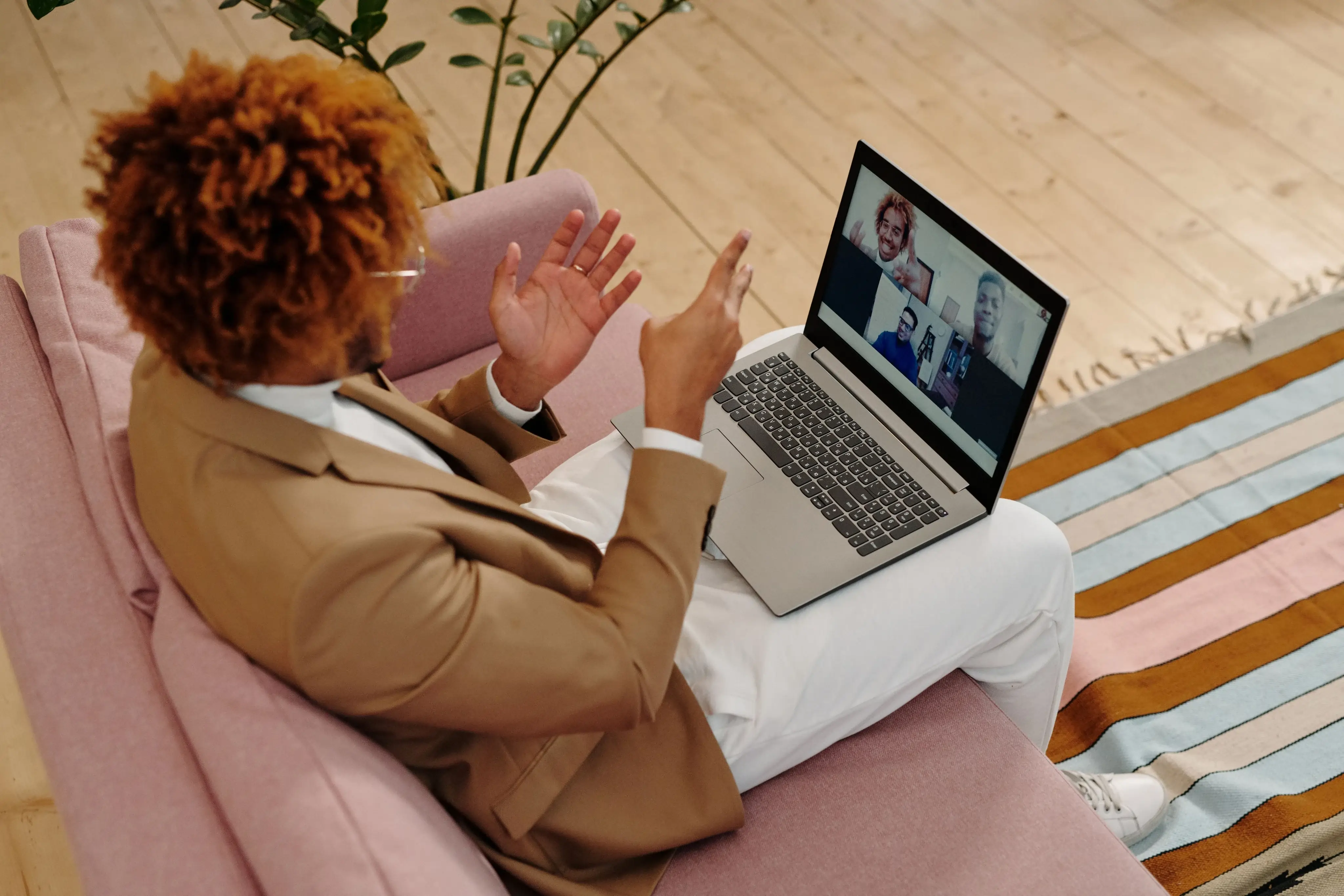Person on couch in brown blazer video chatting with three people on a laptop screen.