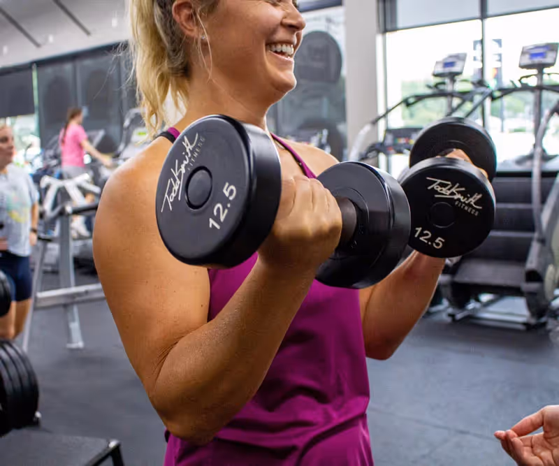 Woman smiling, holding two dumbbells.