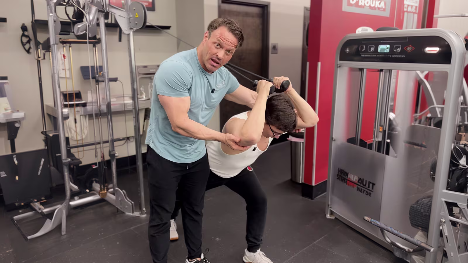 Trainer standing at a member's shoulder during a set — close, watching, not at the front of a room.