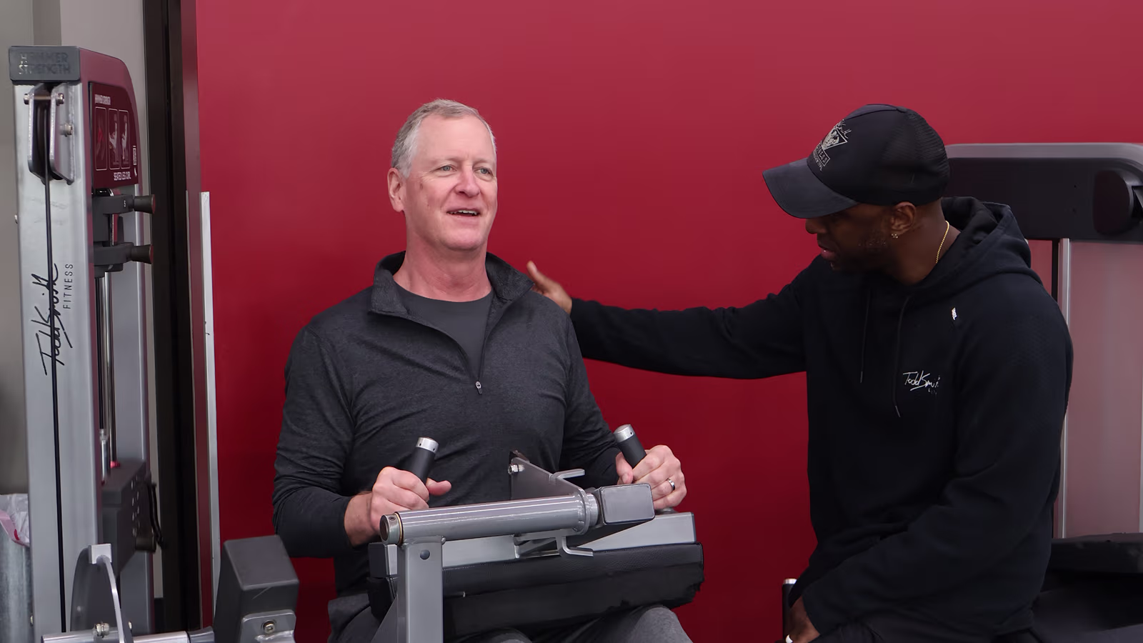 Coach watching a member mid-set — deliberate, controlled. Not a scene of exhaustion.