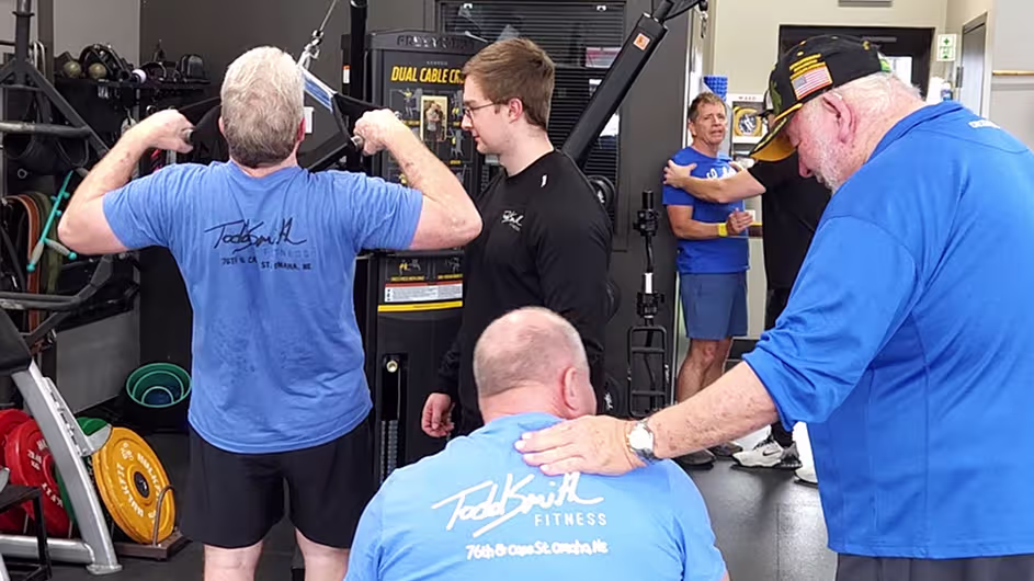 Older adults working out with a trainer at Todd Smith Fitness gym, using cable machines and receiving hands-on guidance.