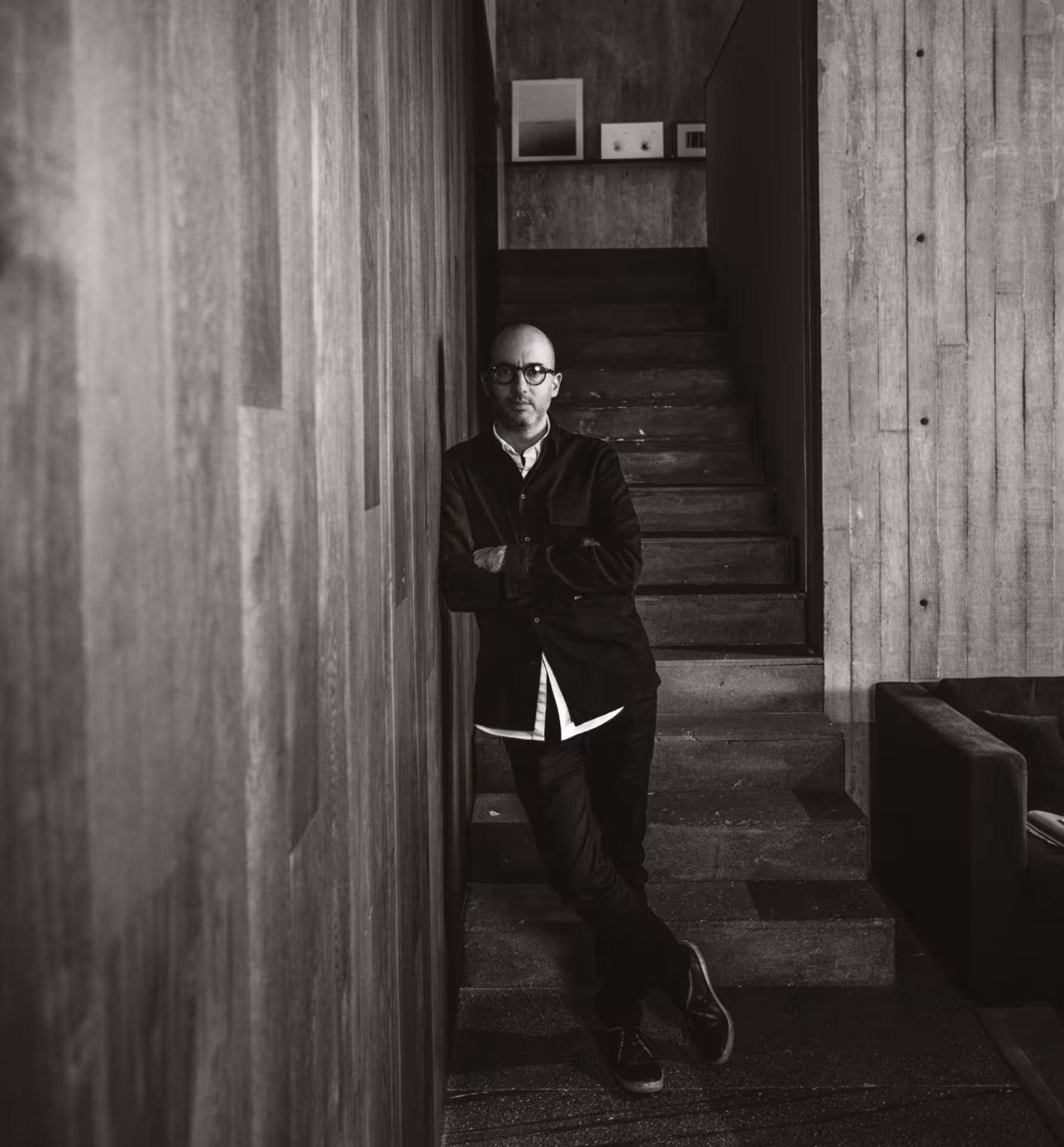 Manuel Cervantes.
Hombre calvo con gafas y ropa oscura apoyado contra una pared de madera frente a unas escaleras de concreto en un espacio interior moderno.