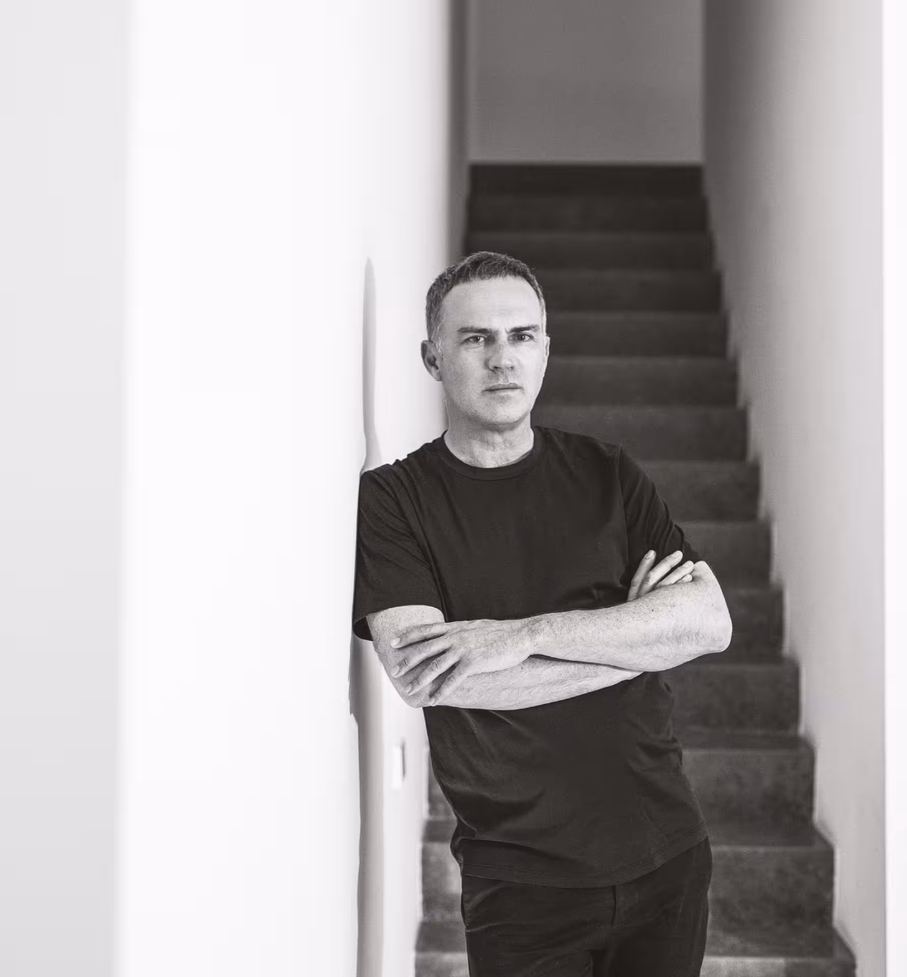 Ramón Esteve.
Hombre de camiseta negra con los brazos cruzados apoyado en la pared frente a una escalera interior.