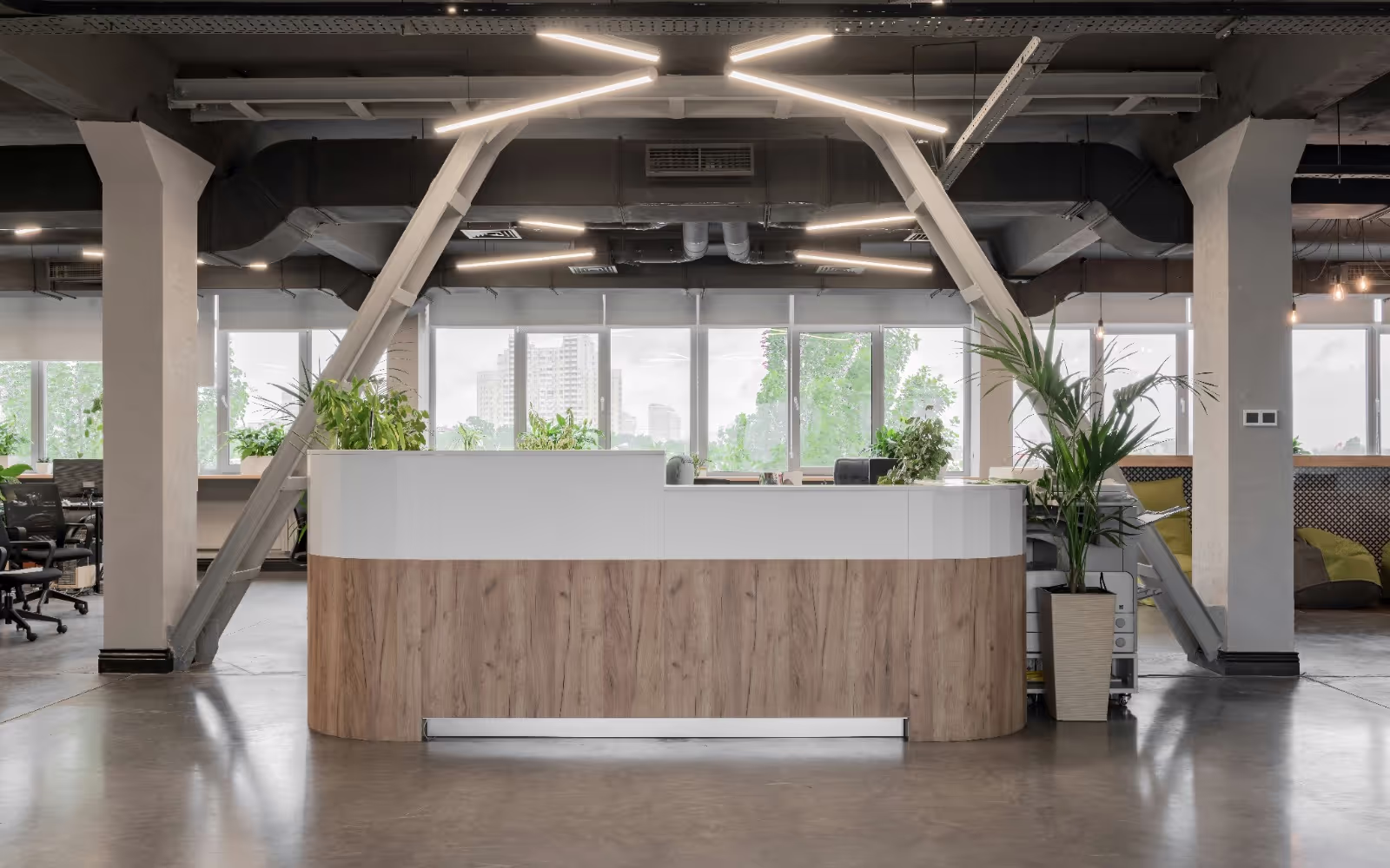 Moderner Empfangstresen in einem offenen Büro mit Blick auf große Fenster und urbanes Grün. Industriedesign mit Holz- und Metallakzenten.