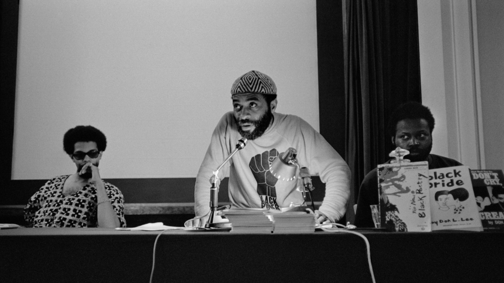 "True North" film still of three men talking at a panel presentation