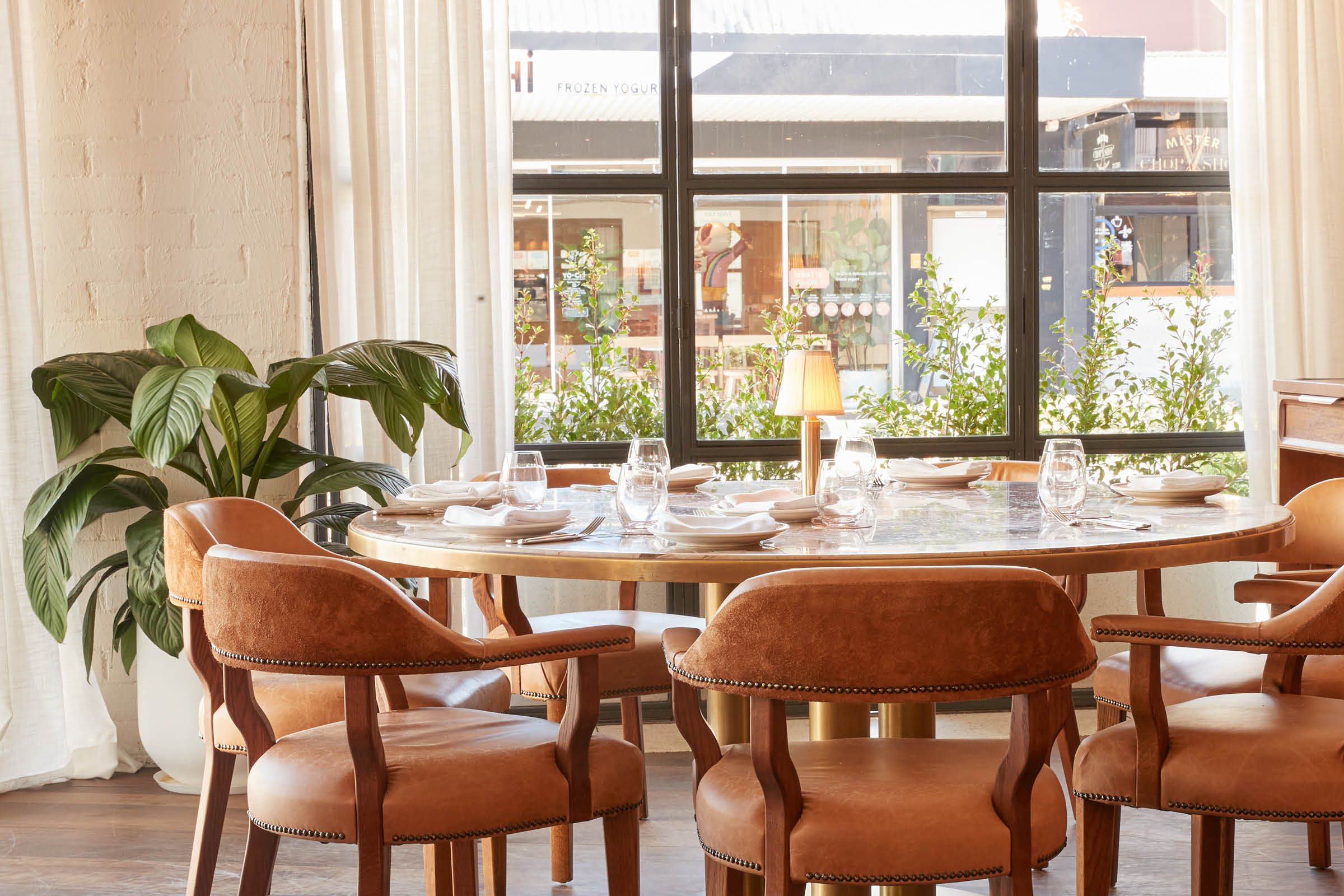 Sunlit window table with tan leather chairs and greenery at Armorica French restaurant in Surry Hills