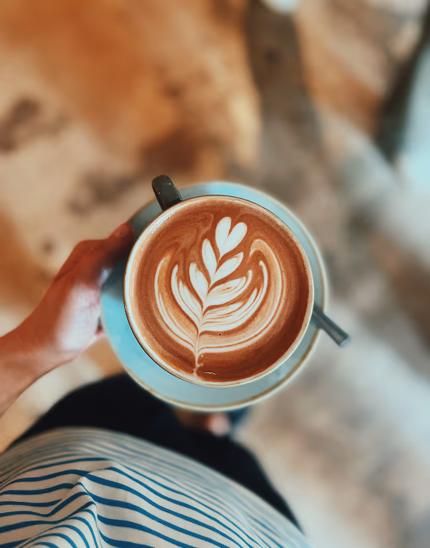 A person holding a cup of coffee with a leaf on it.