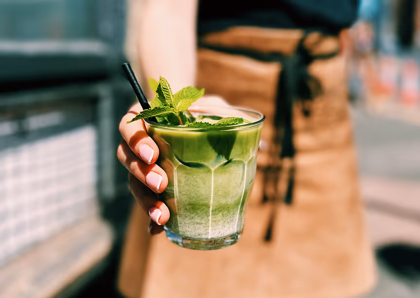 A person holding a green drink in their hand.