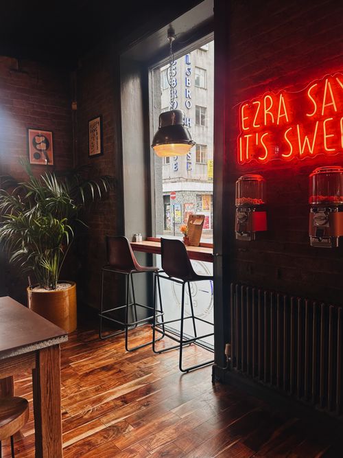 Window bar seats under an Ezra Says It's Sweet neon sign at Ezra & Gil Northern Quarter