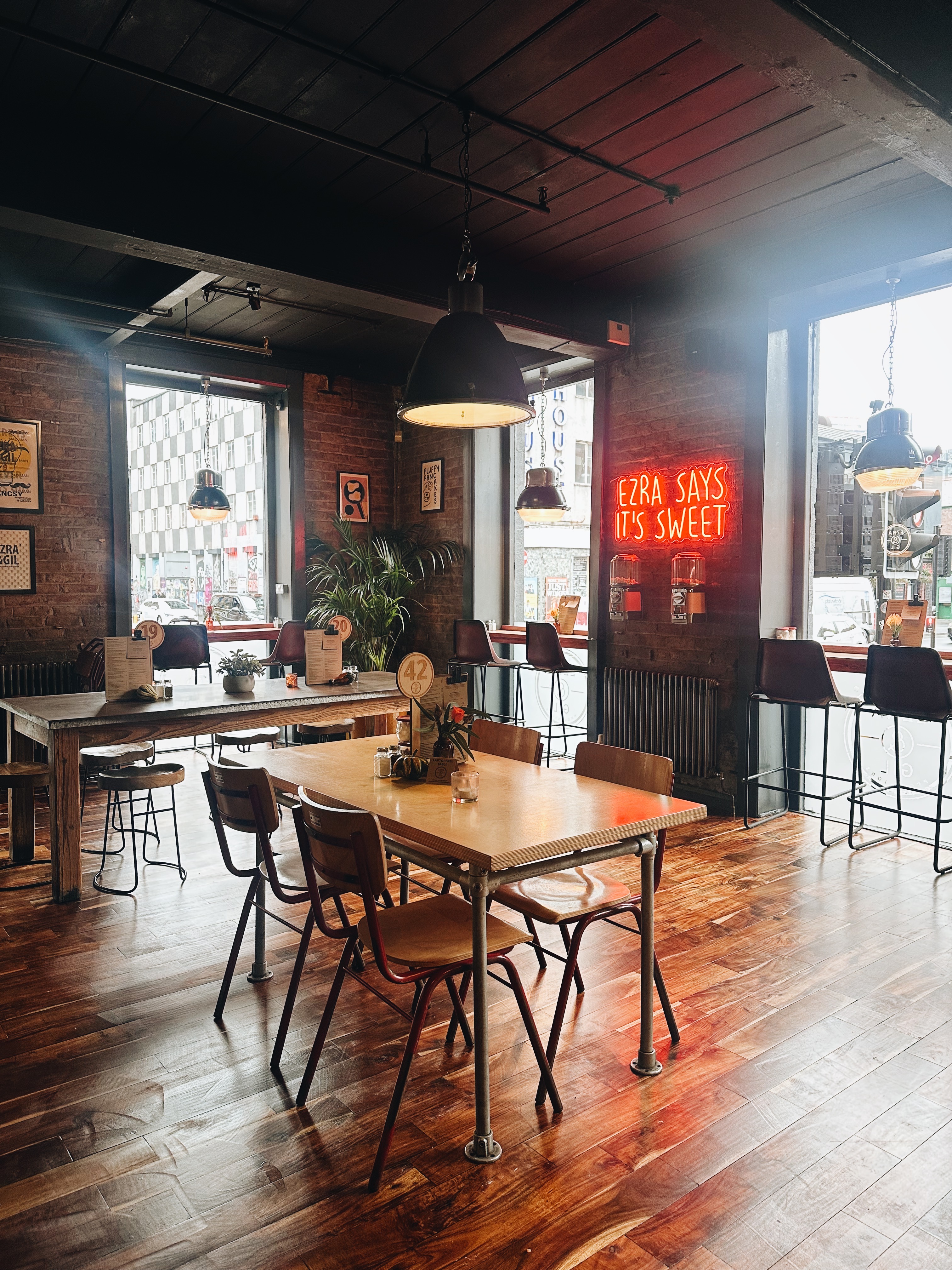 Tables, window bar seating and neon sign in the dining room at Ezra & Gil Northern Quarter