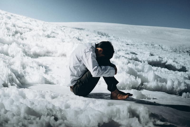 Mann sitz auf Eis und Schnee mit dem Kopf zwischen den Beinen und empfindet eine innerliche Leere, weil er sich nicht wie ein Original fühlt.