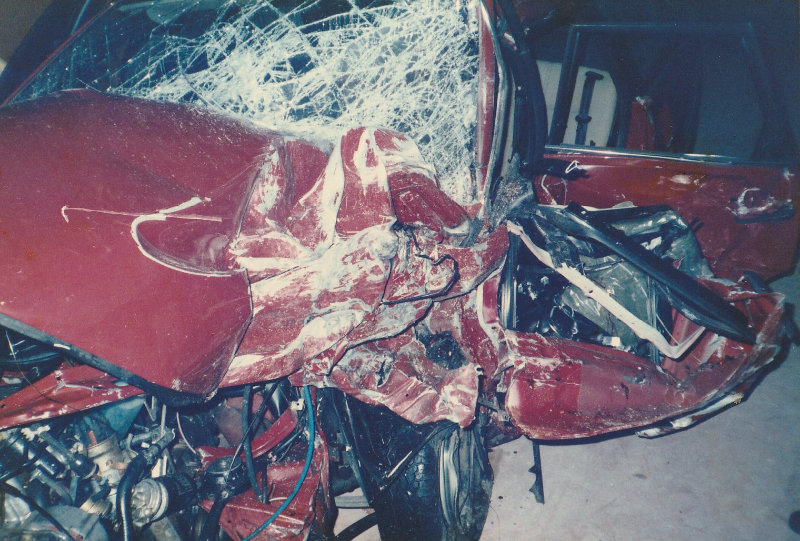 Ein rotes Auto mit Totalschaden nach einem schweren Unfall in Italien, bei dem Dominiks Familie betroffen war – ein Schicksalsschlag, der Trauer und Verlust symbolisiert.