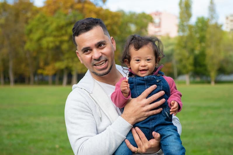 Ein Vater hält stolz sein Kind hoch, beide lachen voller Freude. Dieses Bild veranschaulicht: Wer ist Gott? Gott ist wie ein liebevoller Vater, der seine Kinder annimmt und Freude schenkt.