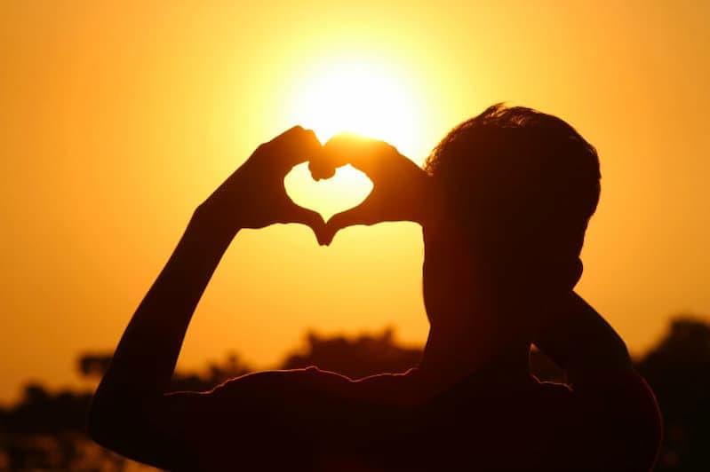 Mann formt mit erhobenen Händen ein Herz zur Sonne als Symbol für Vertrauen auf Gott bei Entscheidungen gemäß Sprüche 3,5-6