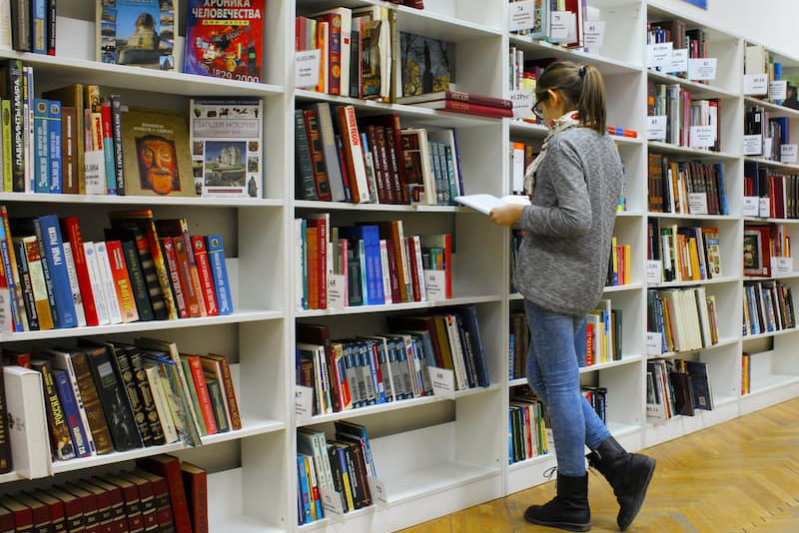 Frau sucht im Bücherregal die passende Bibel – welche Bibelübersetzung ist die richtige