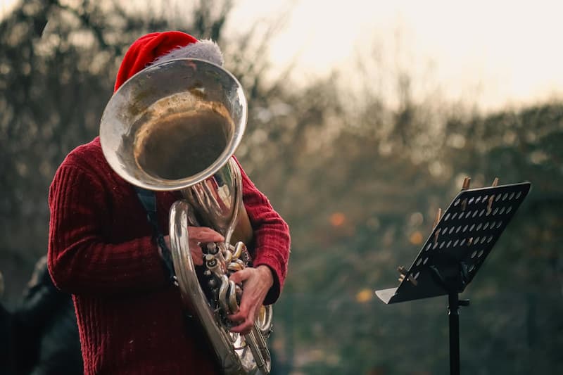 Mann in rotem Weihnachtskleid spielt im Freien Weihnachtslieder auf einer großen Tuba, Notenständer davor, Gesicht teilweise verdeckt