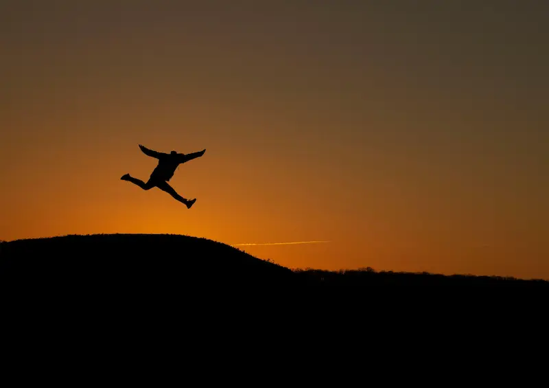 Ein Mensch springt voller Freude bei Abenddämmerung in die Höhe – ein Symbol dafür, dass durch Jesus Christus der Weg zu Gott frei ist.