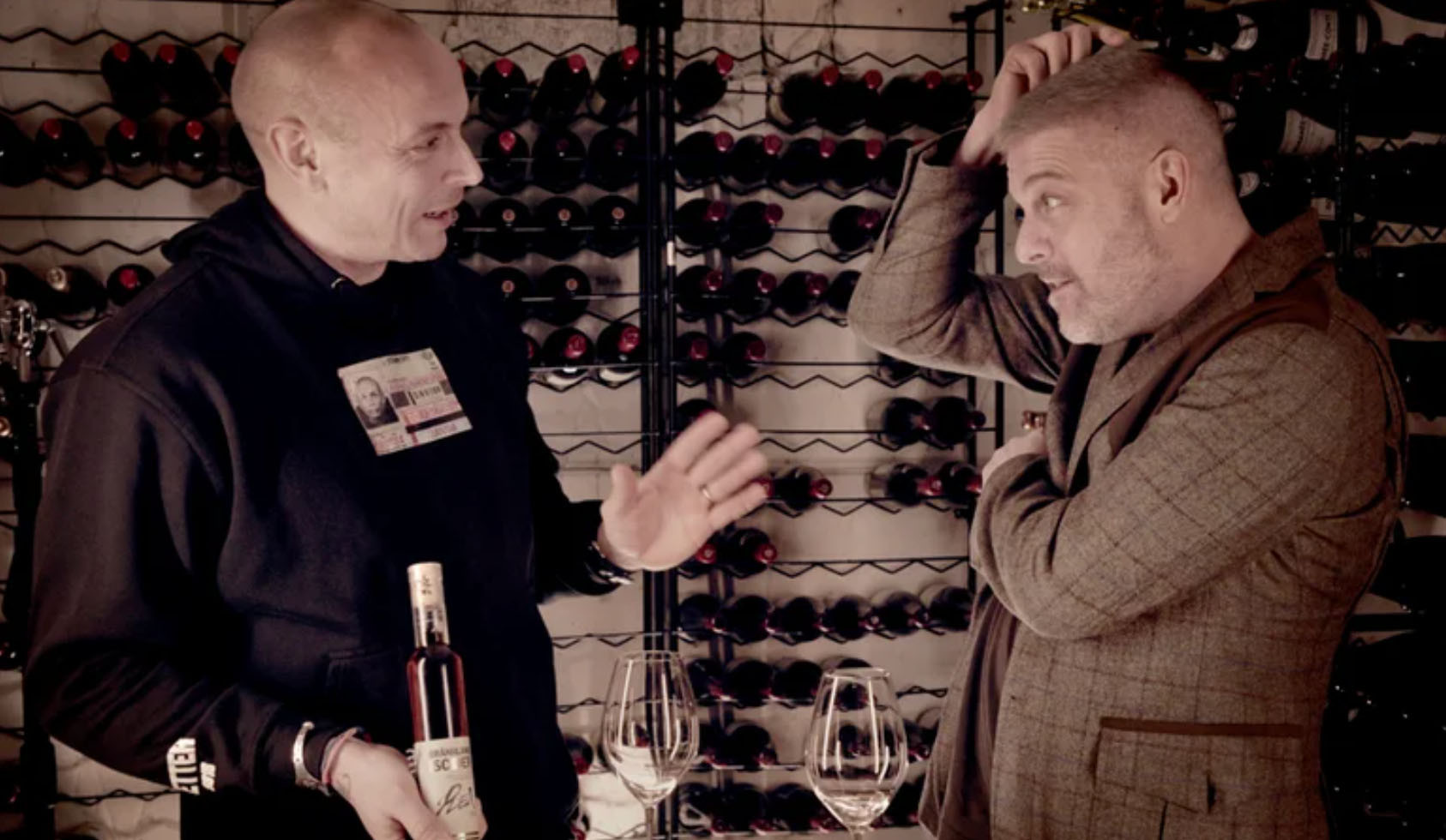 Two people tasting wine in front of a wine rack.