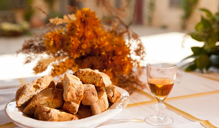 A glass of sweet wine and biscotti on a laid table.
