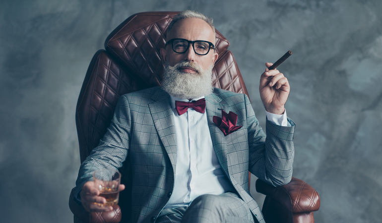 A man holding a wine glass and cigar in an armchair.
