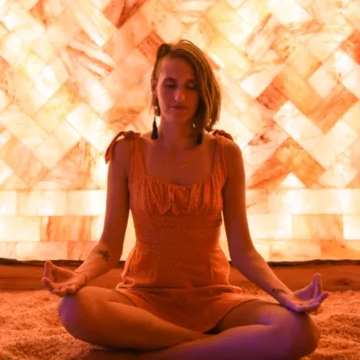 Woman meditating on a salt-covered floor in front of a LED backlit salt panel wall at the Prana Salt Cave - Wilmington, North Carolina.