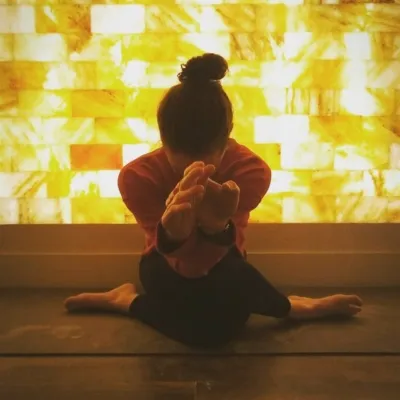 Woman on a black yoga mat doing yoga in front of a LED backlit salt panel at the Sage Blossom Massage - Austin, Texas.