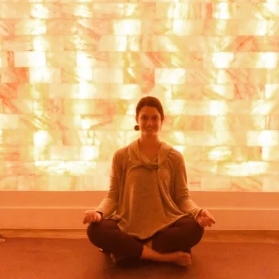 Woman sitting cross-legged smiling in front of a LED backlit salt panel at the Sage Blossom Massage - Austin, Texas.