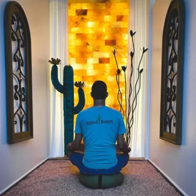 Man meditating on a pillow in a salt room with salt covered floors facing a LED backlit salt panel at the Salted Desert - Peoria, Arizona.