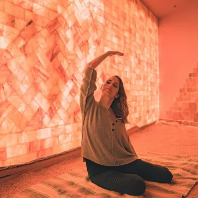 Woman stretching on a blanket on a salt-covered floor in front of a LED backlit salt panel at the Prana Salt Cave & Yoga - Wilmington, NC.