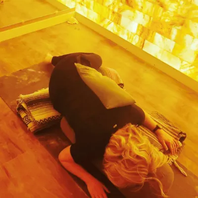 Woman on a yoga mat in front of a mirror with a LED backlit salt panel at Sweet Be Wellness and Skin Clinic - Greeley, Colorado.