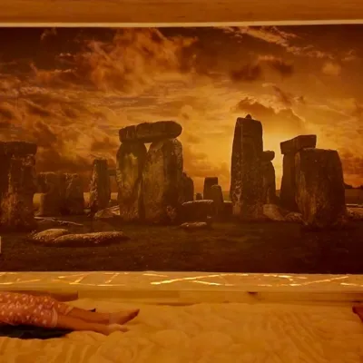 The Salt Cave at Synchronicities Sandy, Utah Two people laying on a salt covered floor in a dim room with a mural of Stonehenge and salt walls
