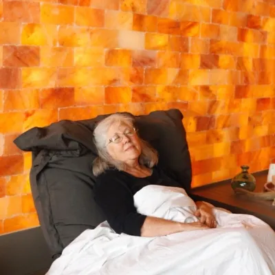 Woman in a black shirt relaxing under a white blanket in front of a Himalayan salt panel wall.
