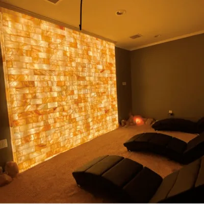 Three black lounge chairs in a salt therapy room on a salt-covered floor facing a LED backlit salt panel wall.
