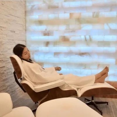 Halo Spa & Salt. Woman relaxes in lounge chair inside of bright, white salt room.