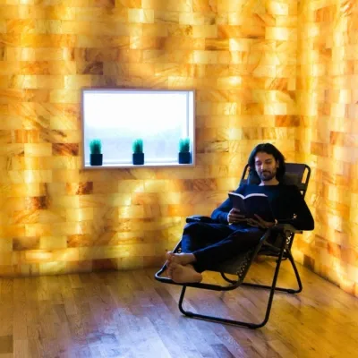 Man reading a book in a reclined chair on wooden floor in front of a backlit Himalayan salt wall at JaiPure Yoga in Montclair, New Jersey