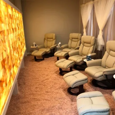 Four tan chairs and footstools on a Himalayan salt-covered floor facing a LED backlit salt brick wall.