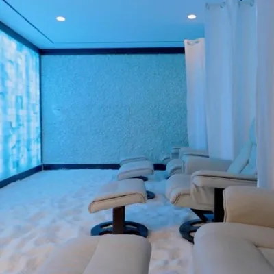 A line of tan chairs with ottomans on Himalayan salt-covered floor facing a blue LED backlit salt brick wall, with another salt wall on the far end of the room