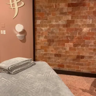 A massage chair with a towl on top in a room with a salt-covered floor and a salt brick wall with the Salt Works and Spa logo on the wall.