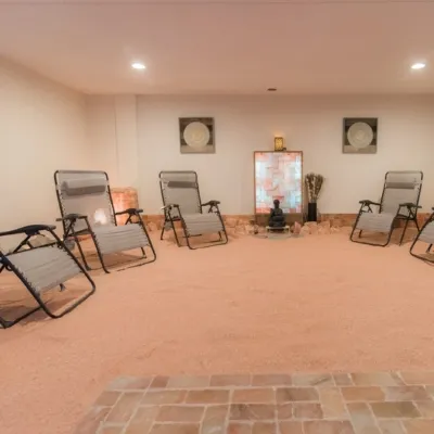 Seven reclining chairs in a room with salt-covered floors and a buddha statue in the far end of the room in front of an LED backlit salt panel