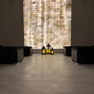 A beautifully LED backlit salt brick wall in an arch shape with three lanterns and four black lounge benches in a white marbled-tiled room