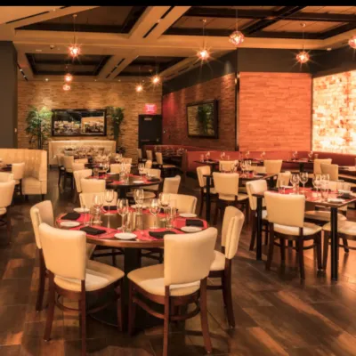 A restaurant dining room with white chairs and tables with a salt brick wall backlit by LED lighting.