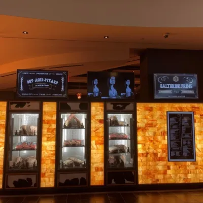 Three fridges with different types of meat displayed in a salt brick wall backlit by LED lighting with a TV above and two signs.
