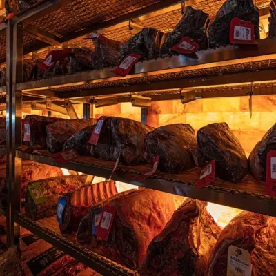 Five shelves with different types of meat with price tags in front of a Himalayan salt paneled wall backlit by orange lighting at Meat On Ocean