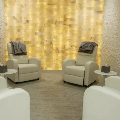 Four white chairs facing each other in a white room with a salt wall backlit by yellow light in Vineyards Country Club in Naples, Florida