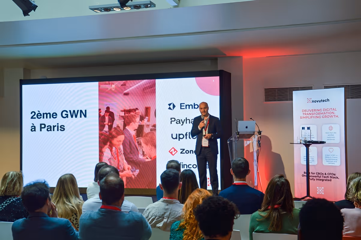 Man holding microphone giving presentation to seated audience at business event in Paris.