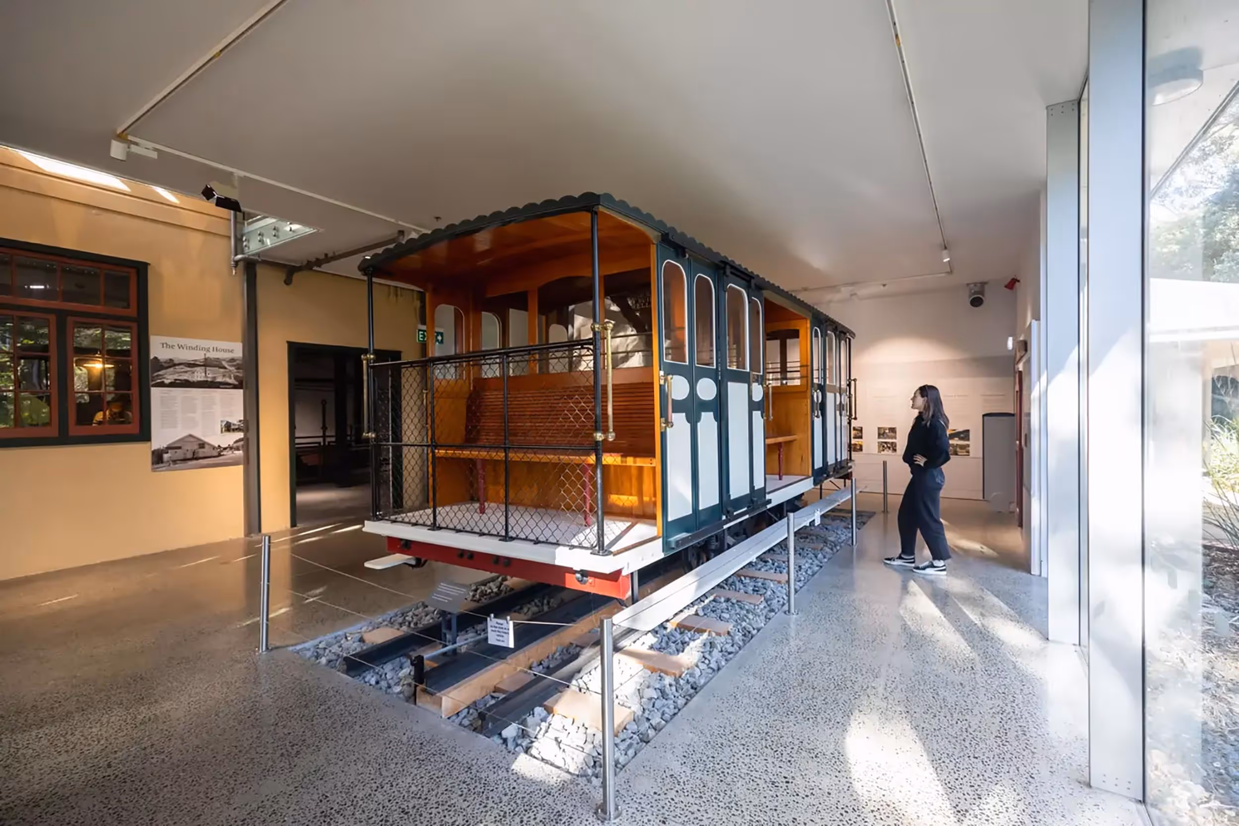Visitor observing an old cable car with wooden benches displayed indoors on short railway tracks.